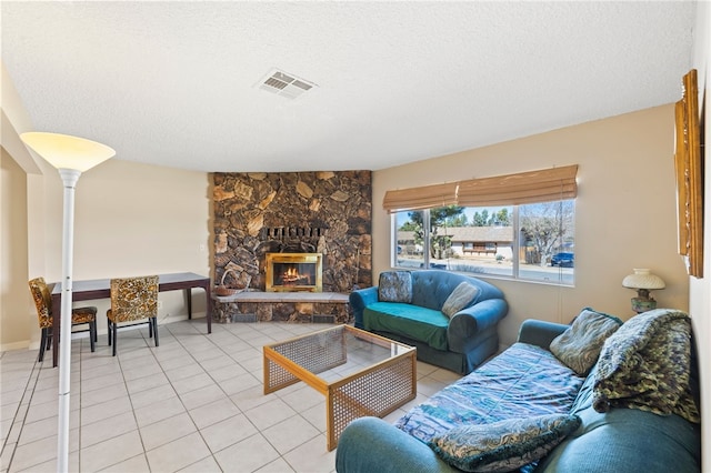 living room featuring light tile patterned floors, visible vents, a textured ceiling, and a stone fireplace