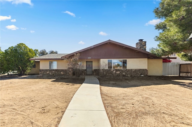 ranch-style house featuring stone siding, a chimney, fence, and stucco siding