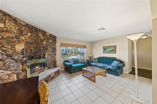 living area featuring light tile patterned floors, visible vents, a textured ceiling, and a stone fireplace