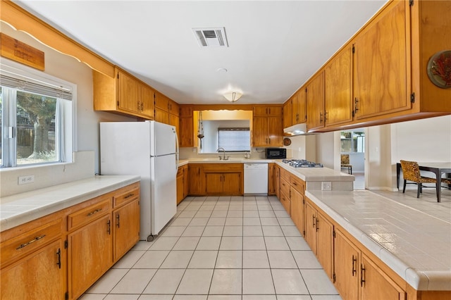 kitchen featuring a peninsula, white appliances, a sink, visible vents, and brown cabinetry