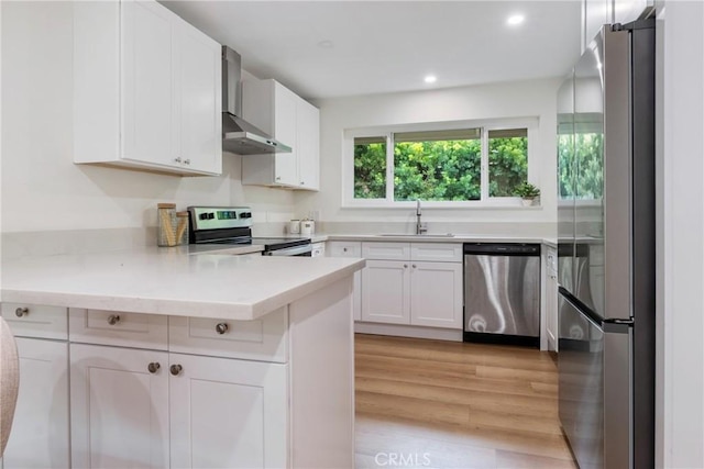 kitchen featuring stainless steel appliances, light countertops, a sink, wall chimney range hood, and a peninsula