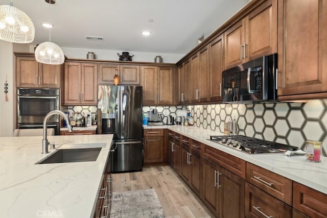 kitchen featuring a sink, light stone counters, light wood-style floors, appliances with stainless steel finishes, and hanging light fixtures