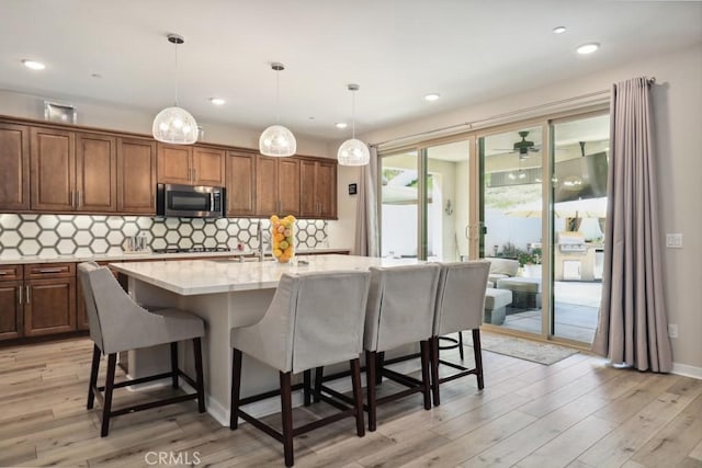 kitchen featuring decorative backsplash, stainless steel microwave, light wood-style floors, and a breakfast bar