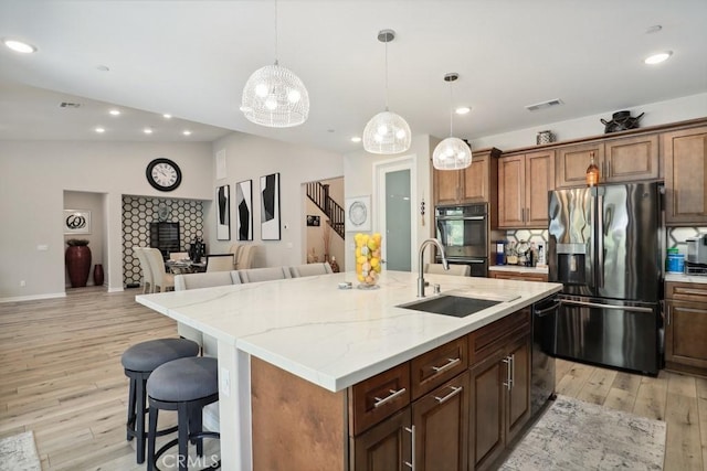 kitchen with visible vents, a kitchen bar, light wood-style flooring, black appliances, and a sink