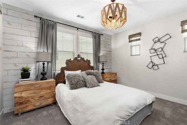 carpeted bedroom with a chandelier, wood walls, visible vents, and baseboards