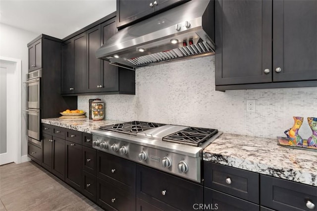 kitchen featuring stainless steel appliances, decorative backsplash, ventilation hood, light stone countertops, and light wood-type flooring