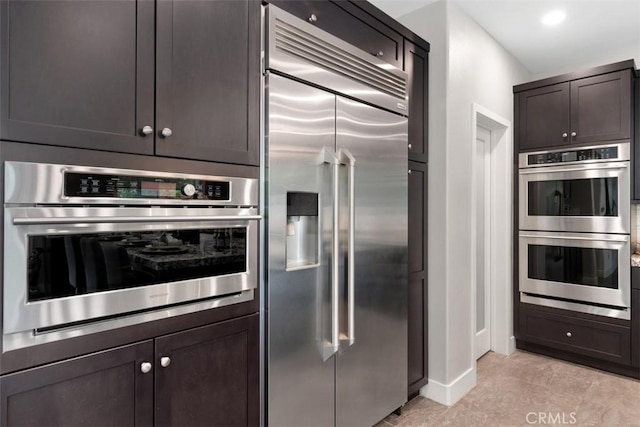 kitchen with stainless steel appliances, dark brown cabinetry, baseboards, and light tile patterned floors