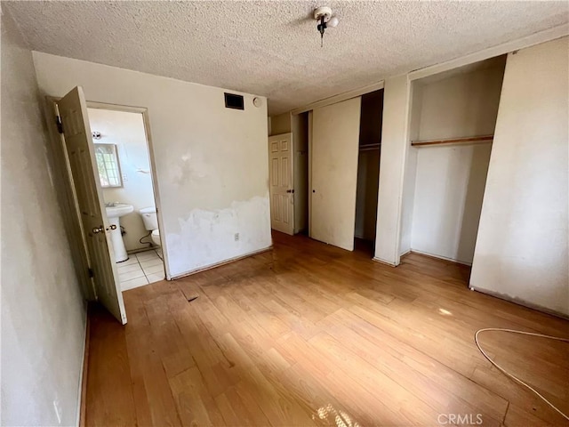 unfurnished bedroom with a textured ceiling, connected bathroom, visible vents, light wood-style floors, and multiple closets