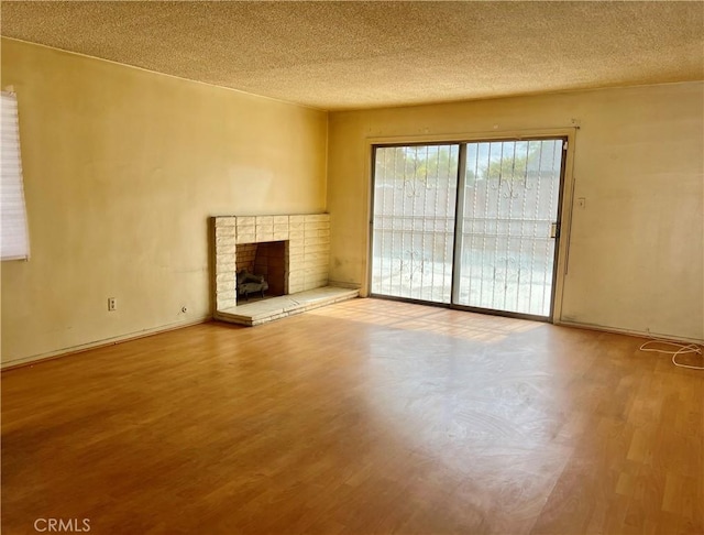 unfurnished living room with a fireplace, a textured ceiling, and wood finished floors