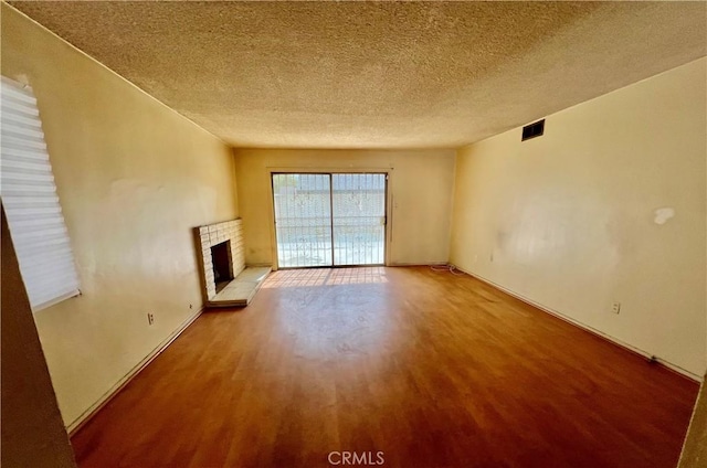 unfurnished living room with a brick fireplace, a textured ceiling, visible vents, and wood finished floors