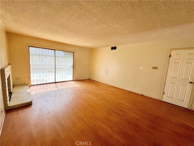 unfurnished living room featuring a textured ceiling, a brick fireplace, wood finished floors, and visible vents