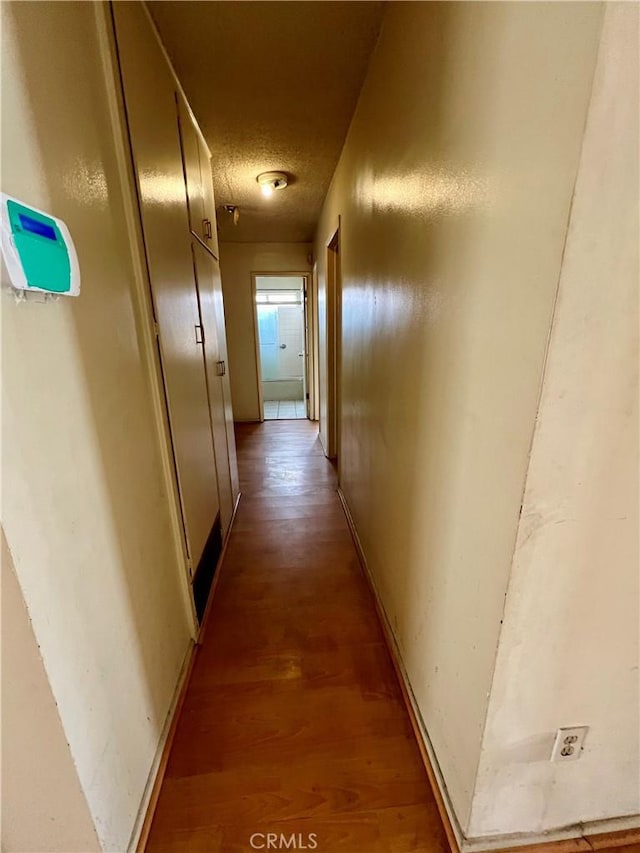 hallway featuring a textured ceiling, baseboards, and wood finished floors