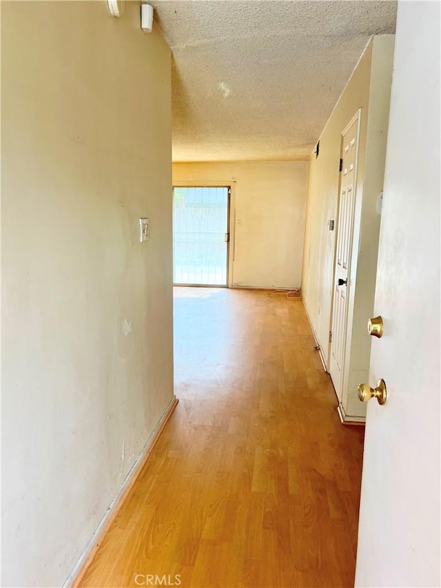 hallway featuring baseboards, light wood-style flooring, and a textured ceiling