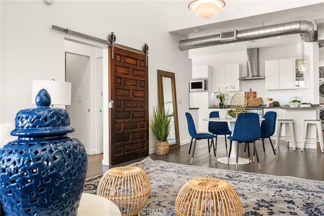 interior space featuring white microwave, stacked washer / drying machine, wall chimney range hood, and dark wood-style flooring