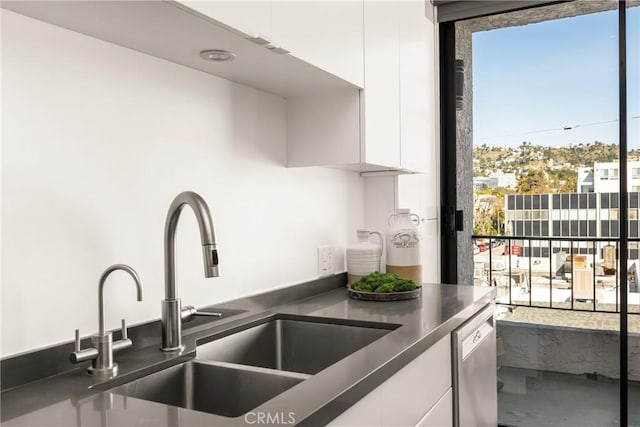 kitchen with dark countertops, a sink, plenty of natural light, white cabinets, and stainless steel dishwasher