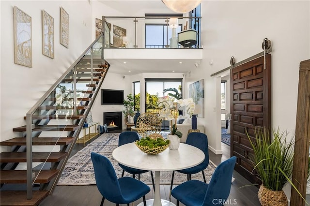 dining area featuring a barn door, stairway, a towering ceiling, and wood finished floors