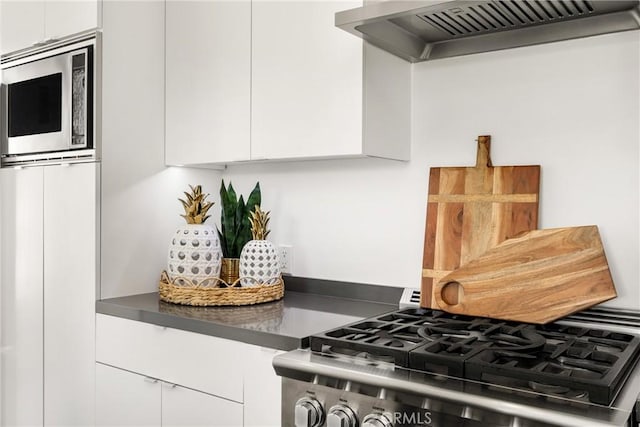 kitchen featuring dark countertops, ventilation hood, stainless steel appliances, white cabinetry, and modern cabinets