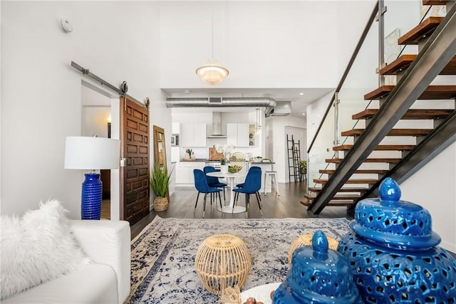 living area featuring a barn door, stairway, dark wood-type flooring, and a towering ceiling