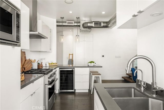 kitchen featuring beverage cooler, a sink, dark countertops, appliances with stainless steel finishes, and wall chimney range hood