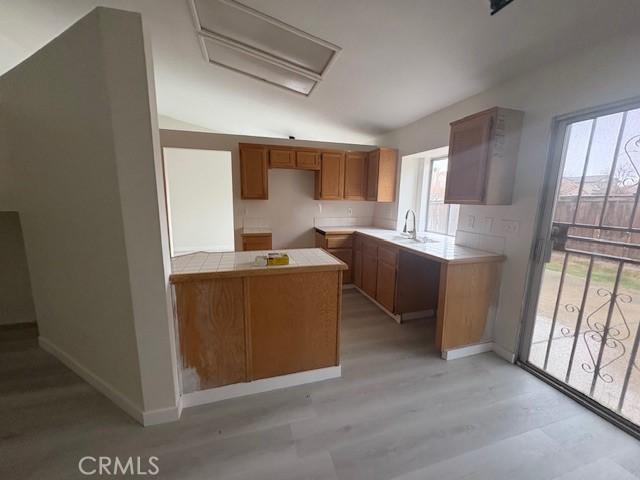 kitchen with tile countertops, light wood-style flooring, brown cabinets, a peninsula, and a sink