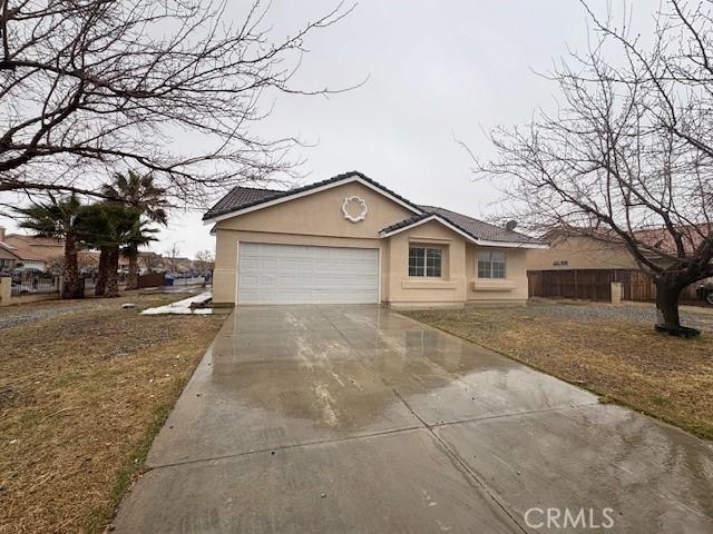 view of front of house with a garage, concrete driveway, a tile roof, fence, and stucco siding