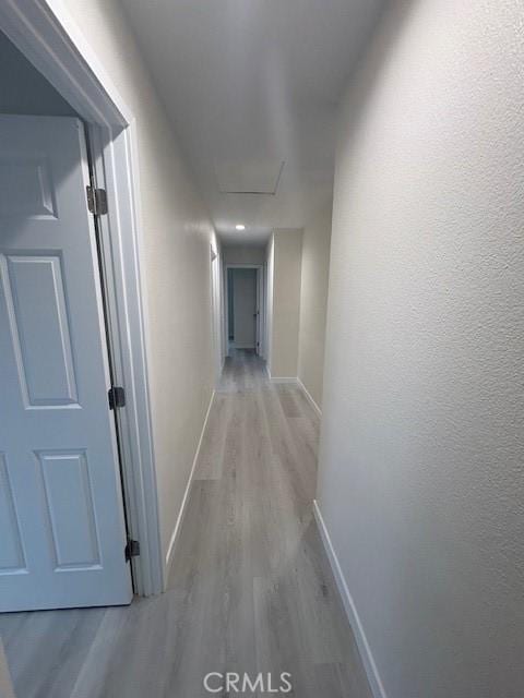 hallway with light wood finished floors, attic access, and baseboards