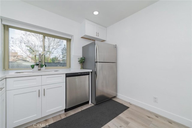 kitchen featuring baseboards, appliances with stainless steel finishes, light countertops, white cabinetry, and a sink