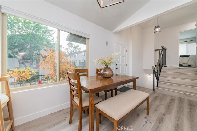 dining space featuring lofted ceiling, baseboards, light wood finished floors, and stairs