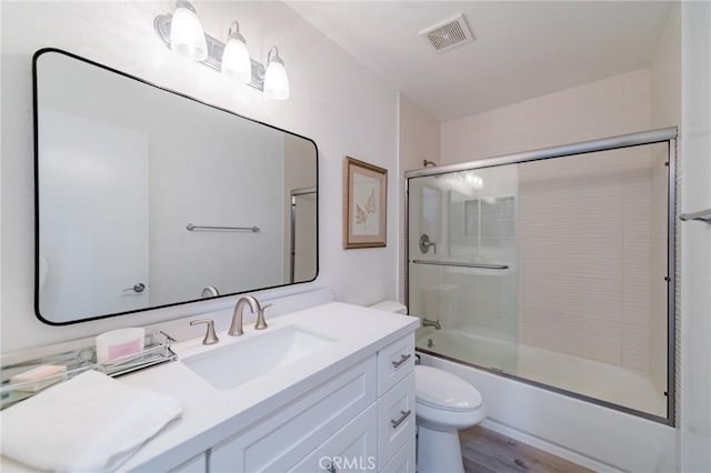 bathroom featuring bath / shower combo with glass door, visible vents, toilet, vanity, and wood finished floors