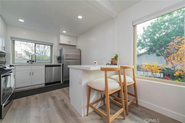 kitchen with stainless steel appliances, light countertops, white cabinetry, light wood-type flooring, and a kitchen bar