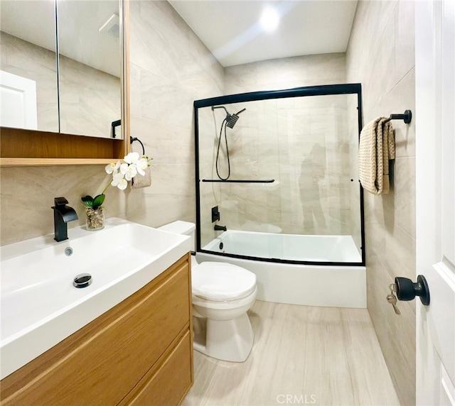 bathroom featuring enclosed tub / shower combo, toilet, tile walls, and vanity