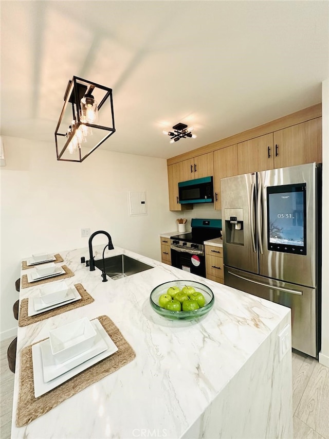 kitchen with light wood-style flooring, a sink, appliances with stainless steel finishes, a peninsula, and light stone countertops