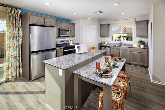 kitchen featuring visible vents, wood finished floors, a center island, light stone countertops, and stainless steel appliances