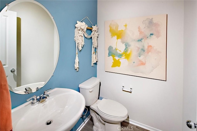 half bath with wood finished floors, a sink, toilet, and baseboards