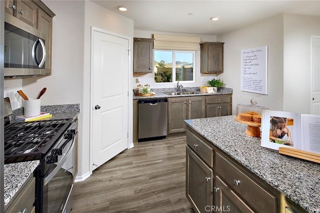 kitchen with appliances with stainless steel finishes, light stone counters, wood finished floors, a sink, and recessed lighting