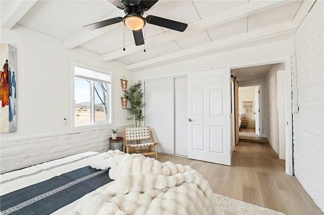 bedroom with brick wall, wood finished floors, a ceiling fan, a closet, and beam ceiling