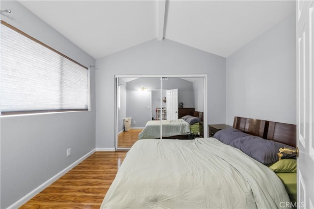 bedroom featuring lofted ceiling with beams, a closet, wood finished floors, and baseboards