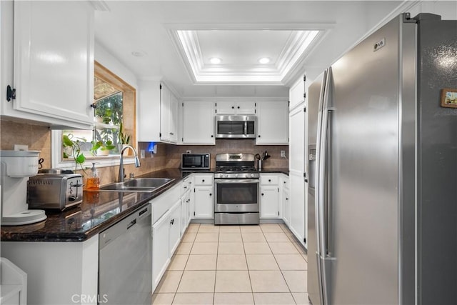 kitchen with a tray ceiling, light tile patterned floors, appliances with stainless steel finishes, ornamental molding, and a sink