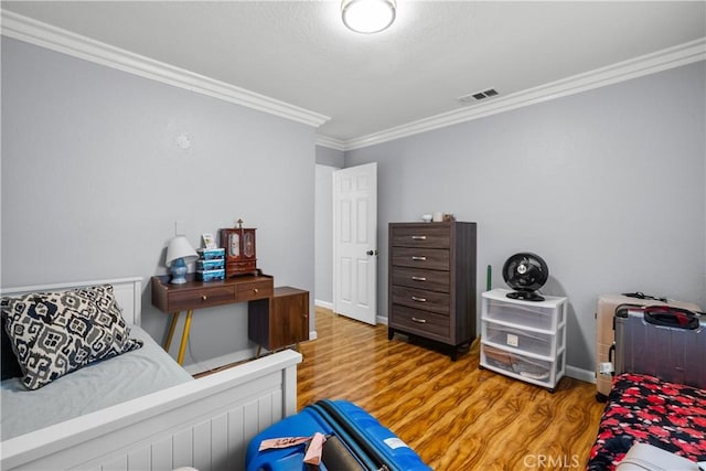 bedroom featuring ornamental molding, wood finished floors, visible vents, and baseboards