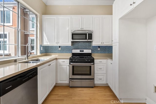 kitchen with light countertops, appliances with stainless steel finishes, light wood-style floors, white cabinets, and a sink