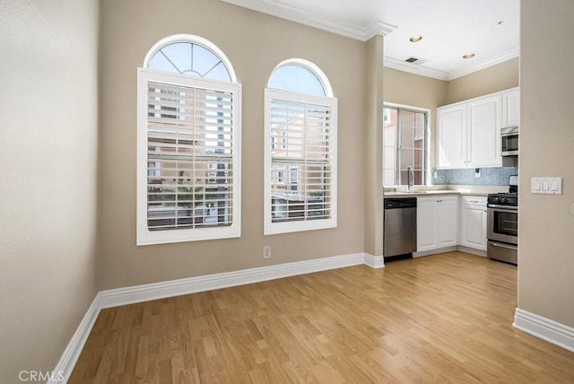 kitchen with appliances with stainless steel finishes, white cabinets, ornamental molding, and baseboards