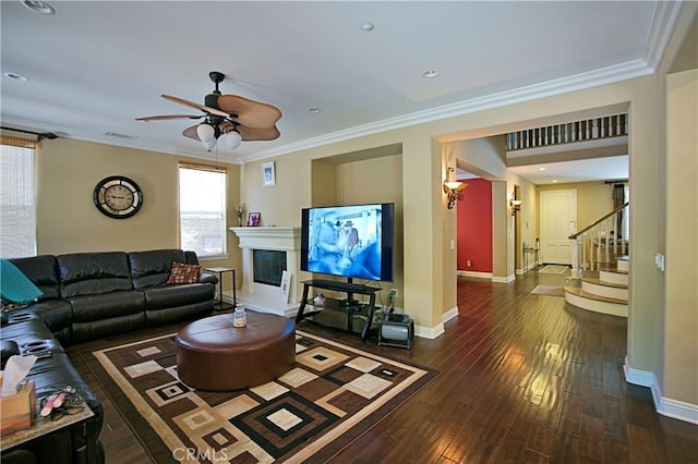 living area featuring baseboards, a glass covered fireplace, ornamental molding, hardwood / wood-style floors, and stairs