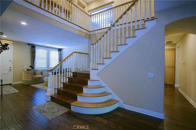 stairway featuring arched walkways, wood-type flooring, visible vents, a high ceiling, and baseboards