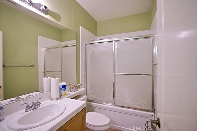 bathroom featuring toilet, shower / bath combination with glass door, and vanity