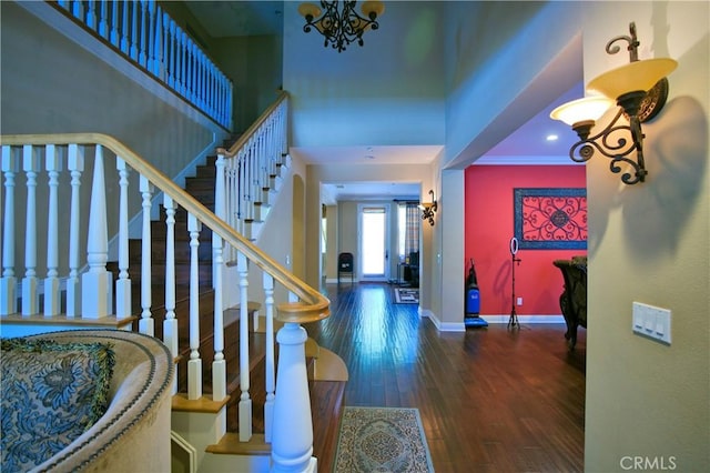 entryway featuring a notable chandelier, wood finished floors, baseboards, stairs, and crown molding