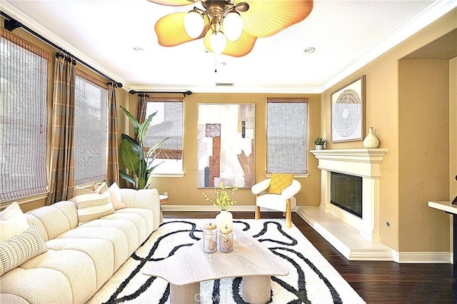 living area featuring crown molding, a ceiling fan, wood finished floors, a glass covered fireplace, and baseboards
