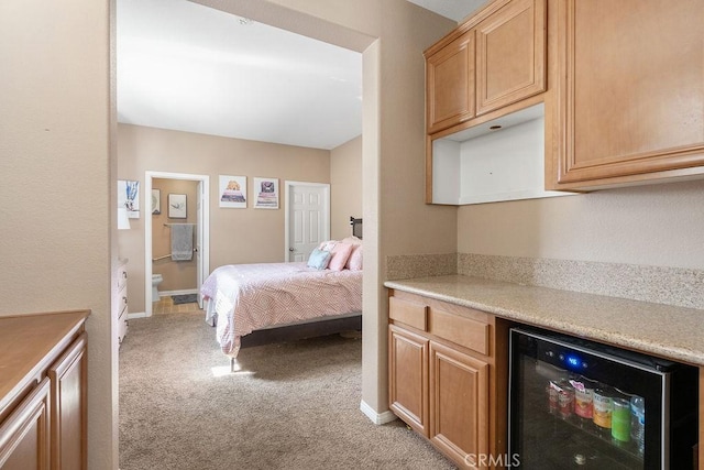 bedroom with ensuite bath, wine cooler, light colored carpet, and baseboards