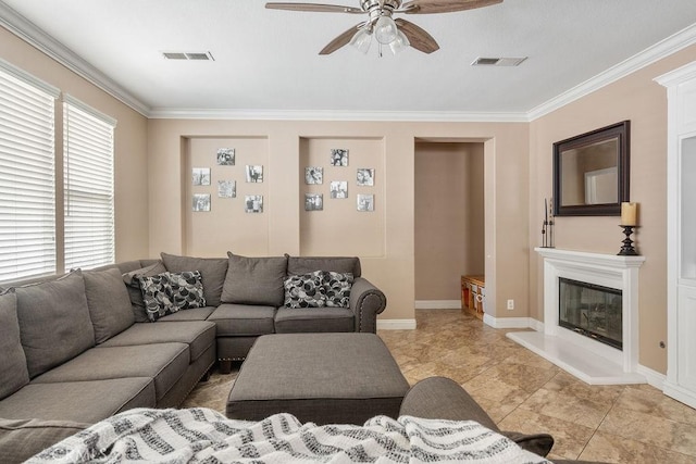 living room featuring a glass covered fireplace, crown molding, visible vents, and ceiling fan