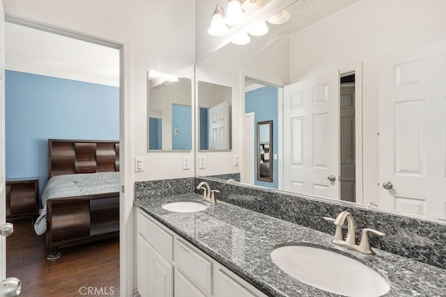 ensuite bathroom with a sink, wood finished floors, double vanity, and crown molding