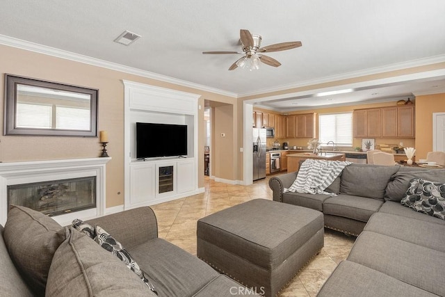 living area featuring visible vents, ceiling fan, baseboards, ornamental molding, and a glass covered fireplace